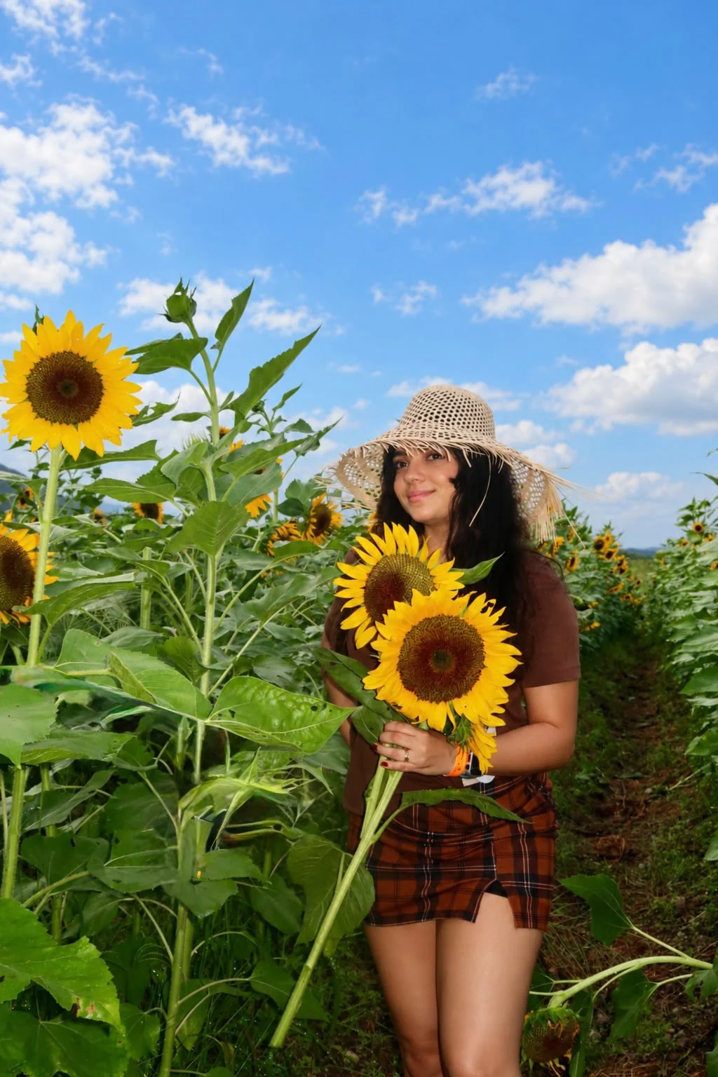 Wileini con sombrero sosteniendo girasoles en un campo de flores